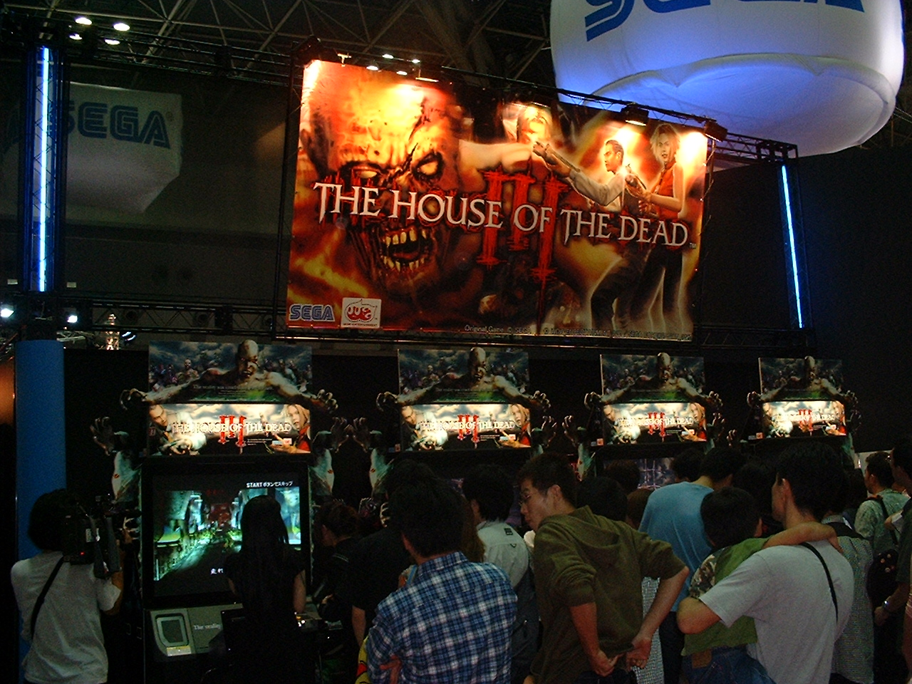 people crowd around demos of the house of the dead 3 under a large logo poster