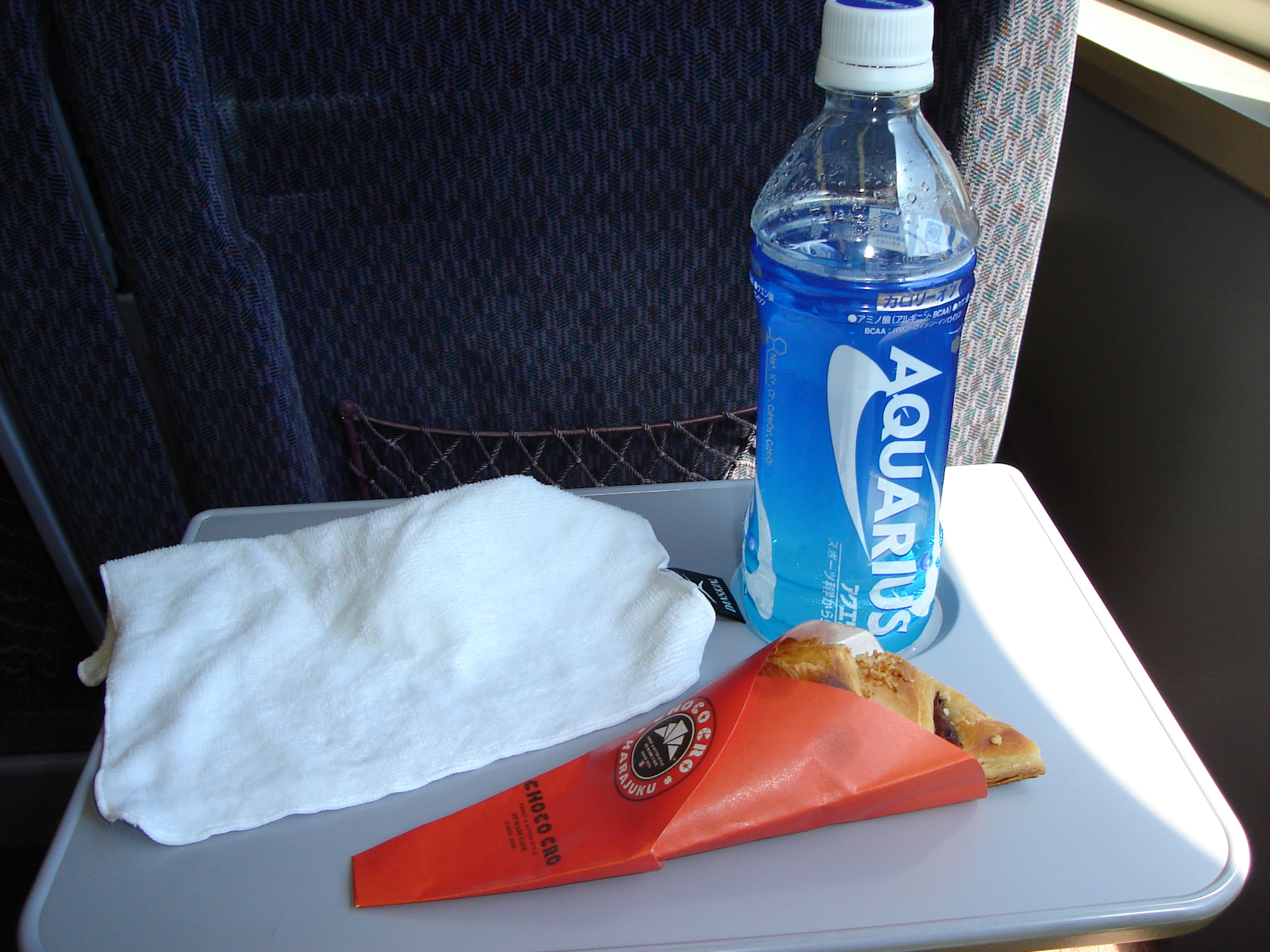 train seat table with a croissant in a wrapper and a bottle of aquarius drink