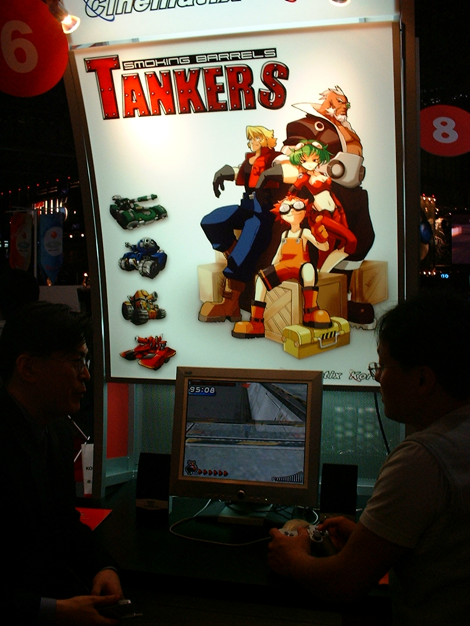 a japanese man plays a game near a poster for tankers showing some characters