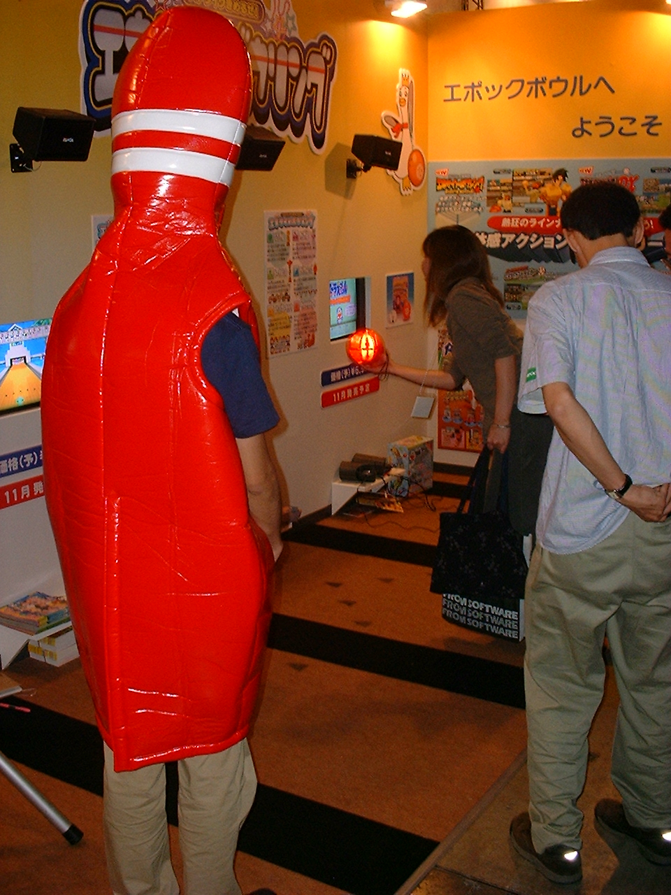 a person in a red bowling pin costume watches people try a game