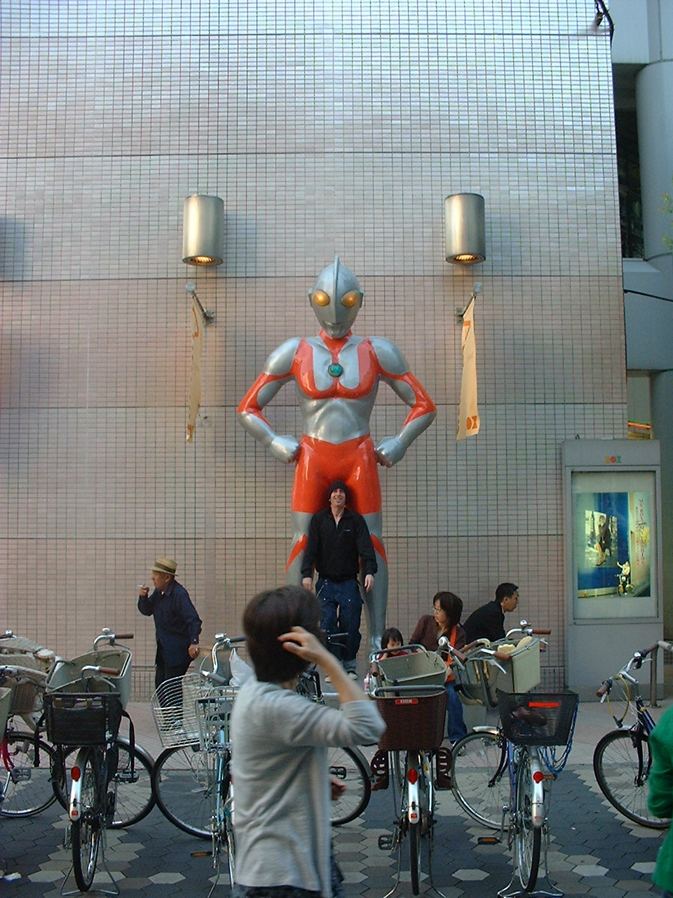 a clean shaven white man stands in front of an ultraman statue