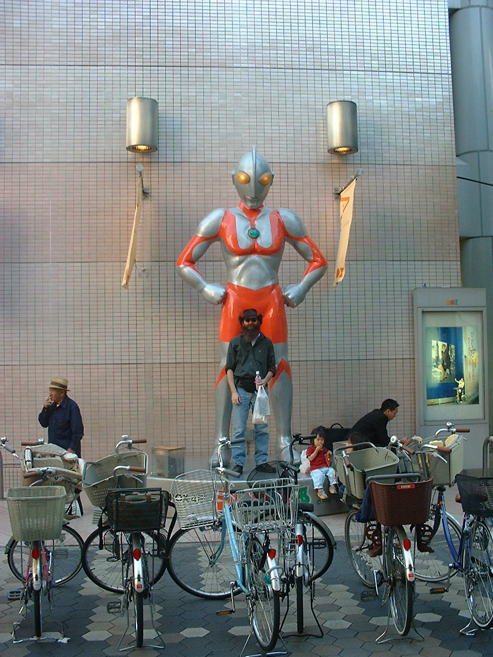 a bearded white man stands in front of an ultraman statue