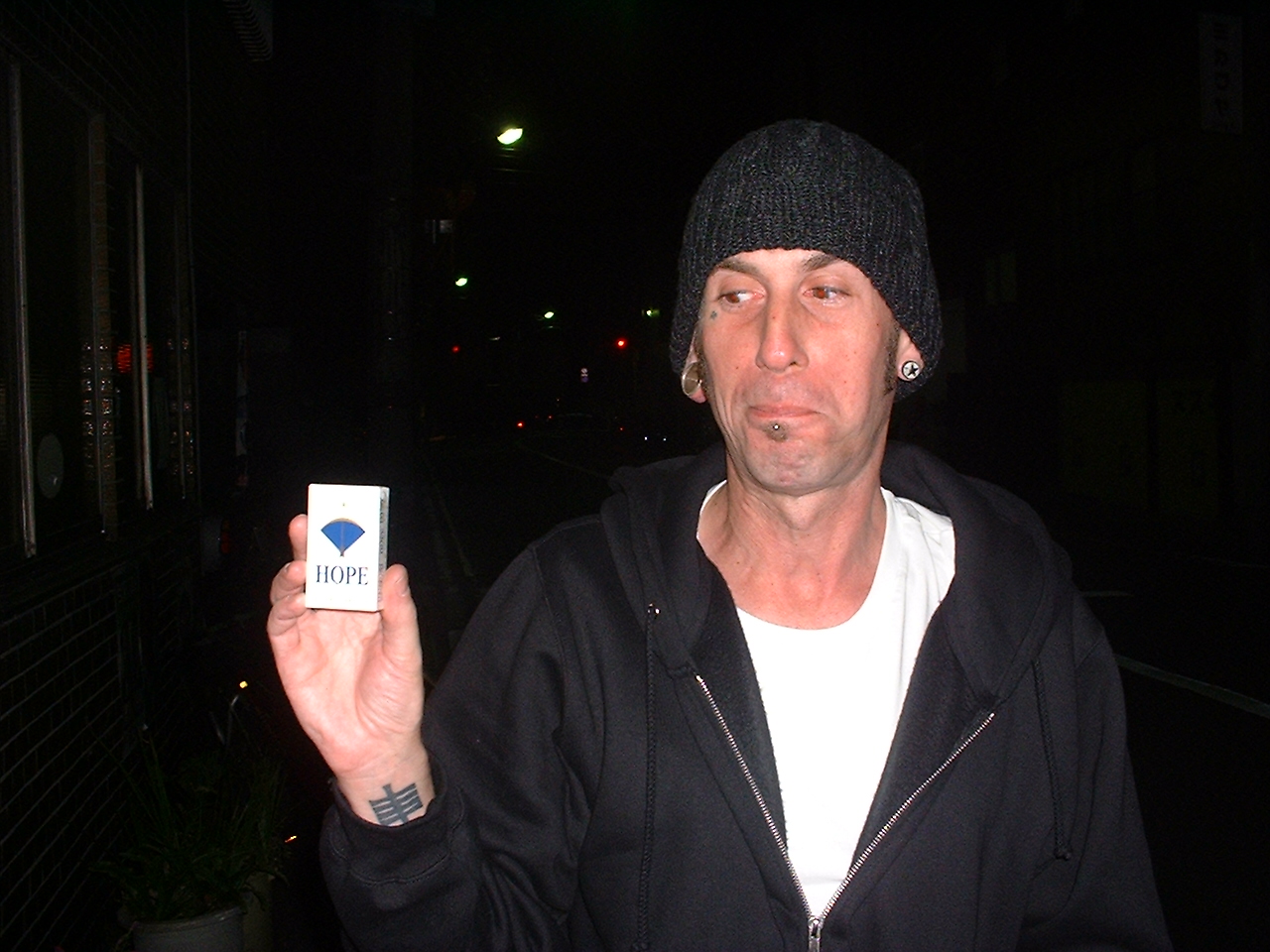 a caucasian man gimaces as he holds up a pack of cigarettes called hope
