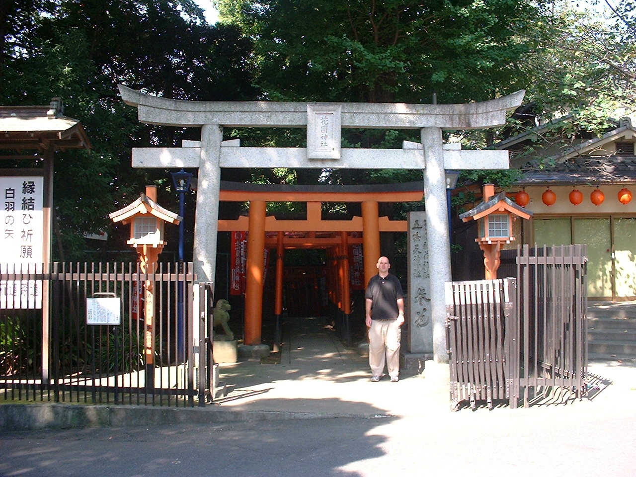 a white man stands near a stone torii gate that leads to some wooden vermillion ones on shrine grounds