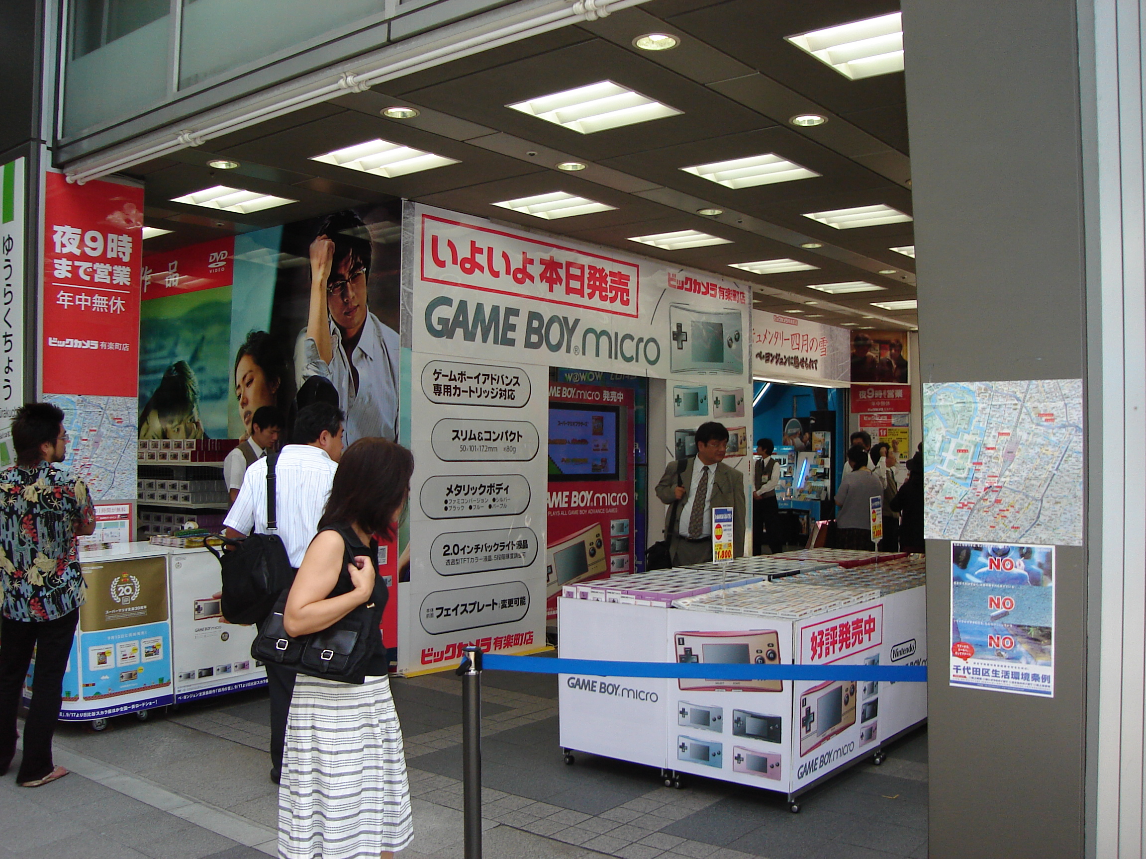 a woman looks curiously at a display and signs for gameboy micro at a store entrance
