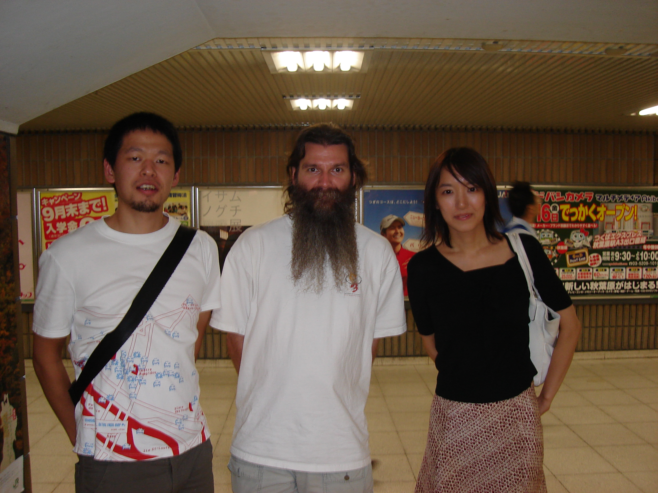a caucasian man with a long dark beard flanked by a young japanese couple