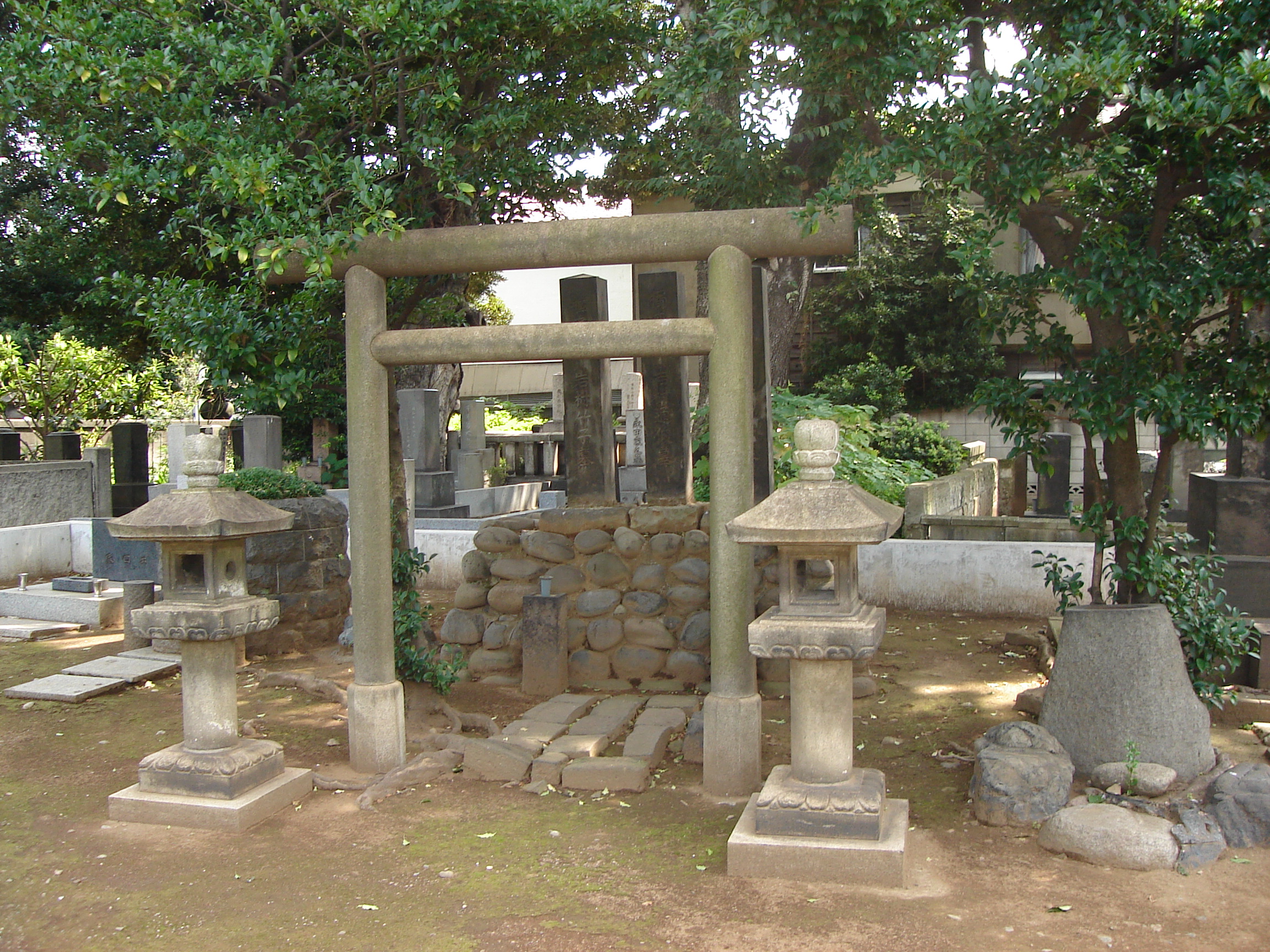 a small torii gate flanked by stone lanterns leads to a stone burial mound