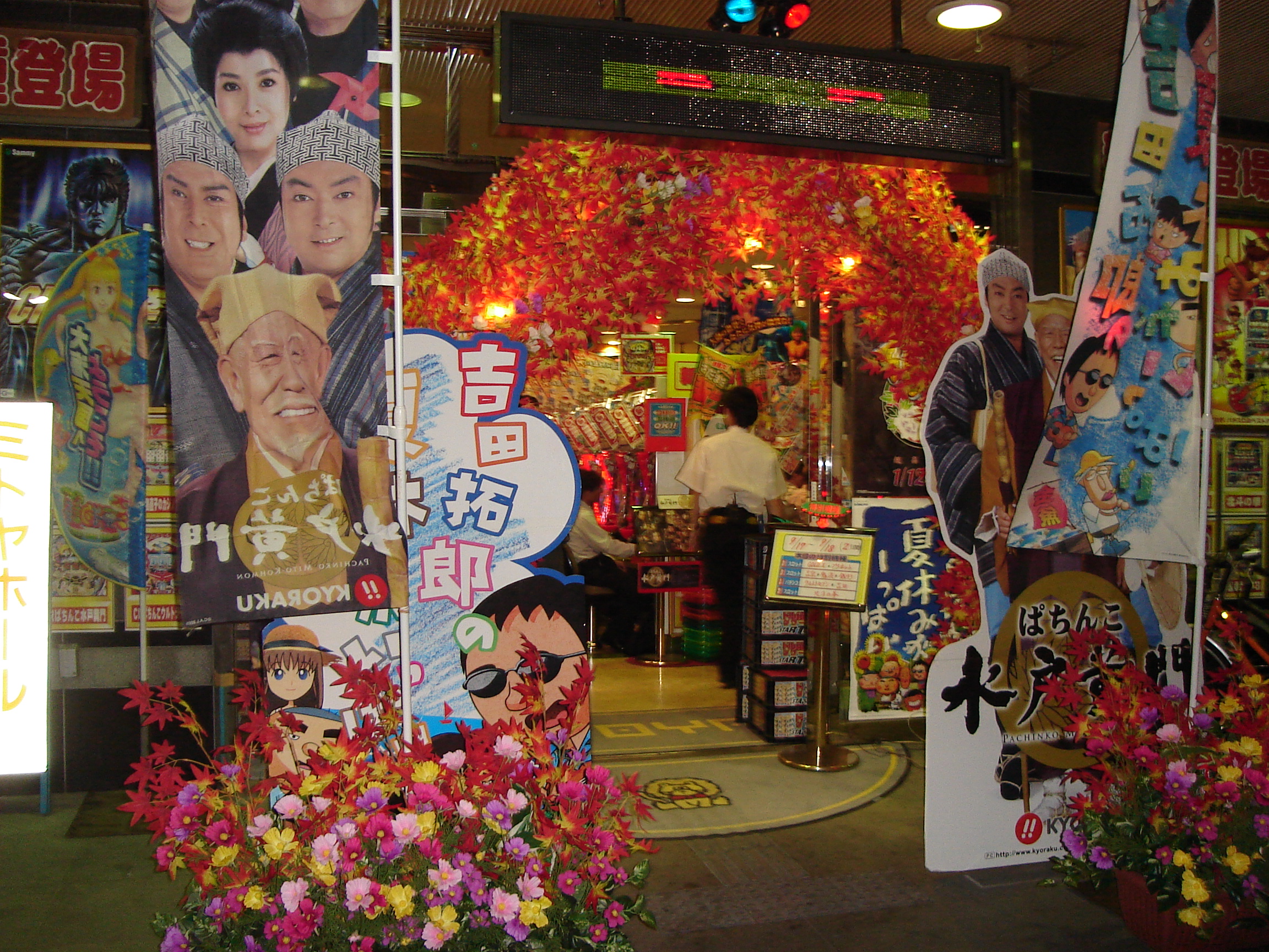 the entrance to a pachinko parlour is crowded with bright signs and baskets of flowers