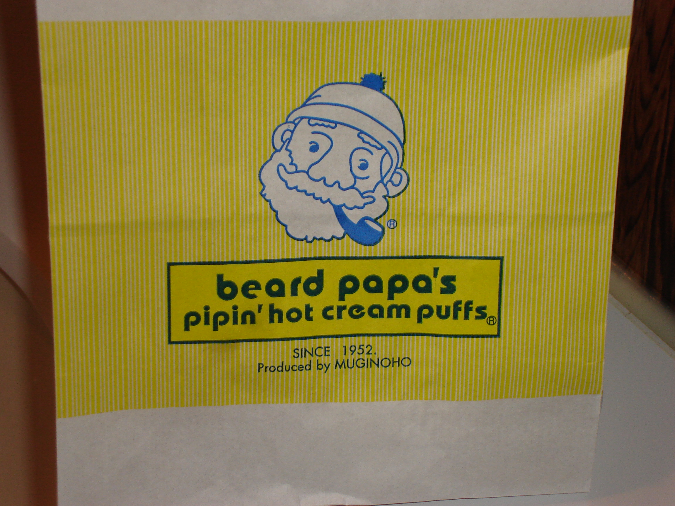a paper bag from beard papa's pipin' hot cream puffs featurs an illustrated bearded man with a pipe