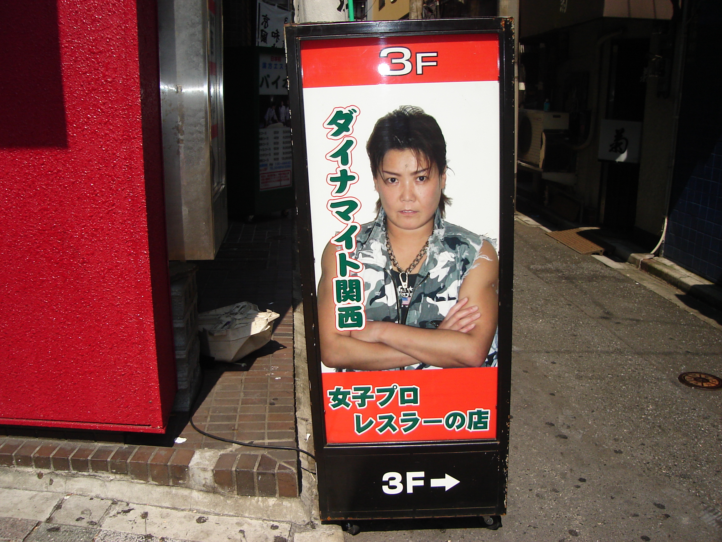 a sign reads 3F and dynamite in japanese with a photo of a short-haired woman in an urban camoflauge vest