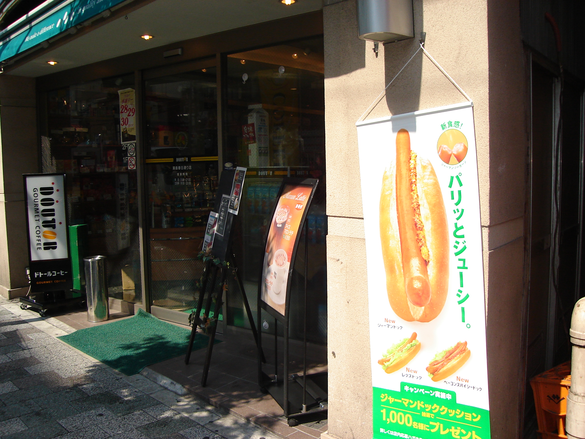 a sign outside a store shows hot dogs, one with lettuce added