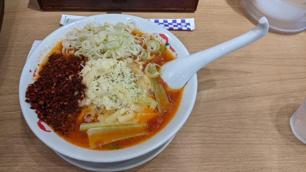 Bowl of ramen with red broth and several tablespoons of chiliflakes covering part of it