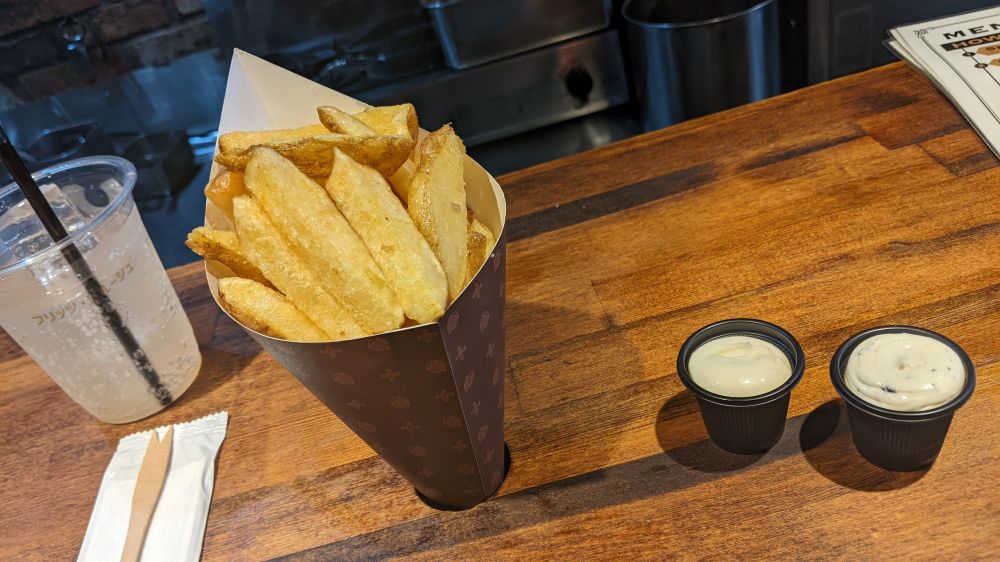 A drink, a cone full of frites, and two cups of sauce